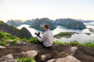 Man sitting on a cliff overlooking a scenic fjord landscape.