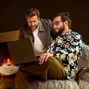 Two men looking at a laptop near a fireplace